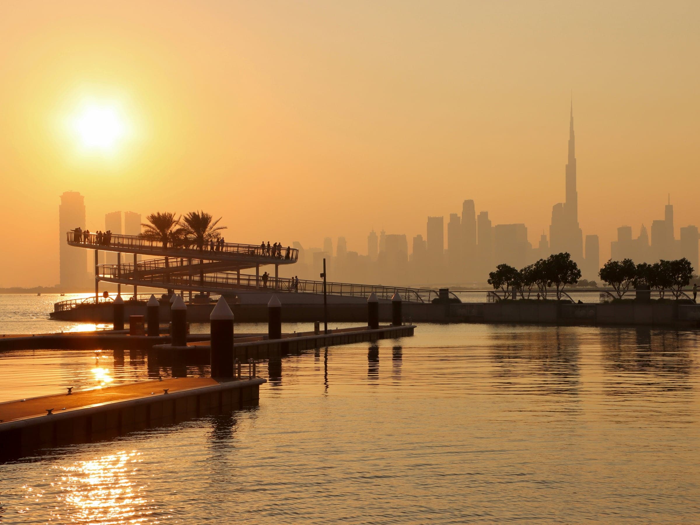 Sunset over the Dubai Creek Harbour waterfront boardwalk, with the Burj Khalifa across the water