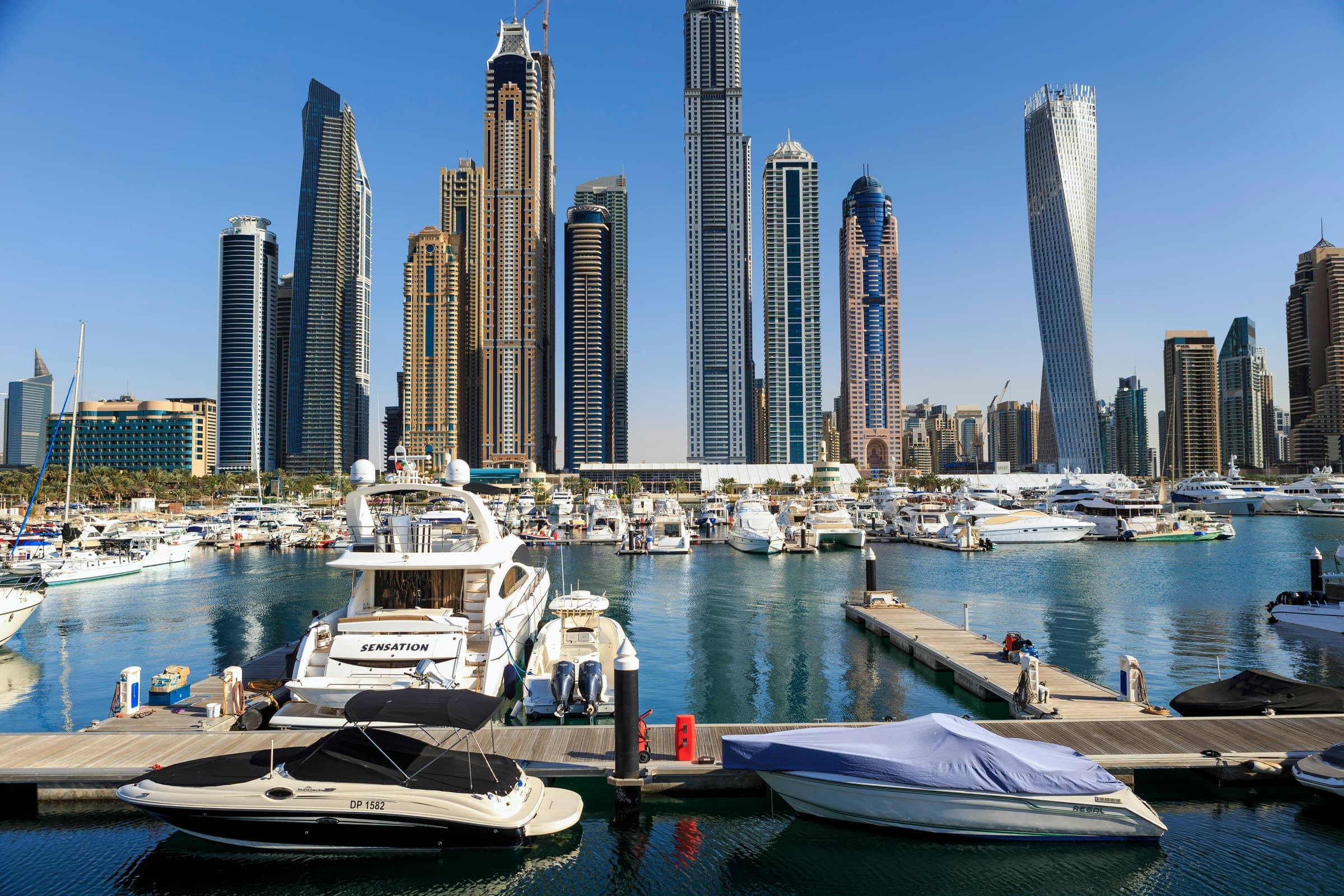 Yachts moored in Dubai Marina beneath the district's landmark towers, including the twisting Cayan Tower