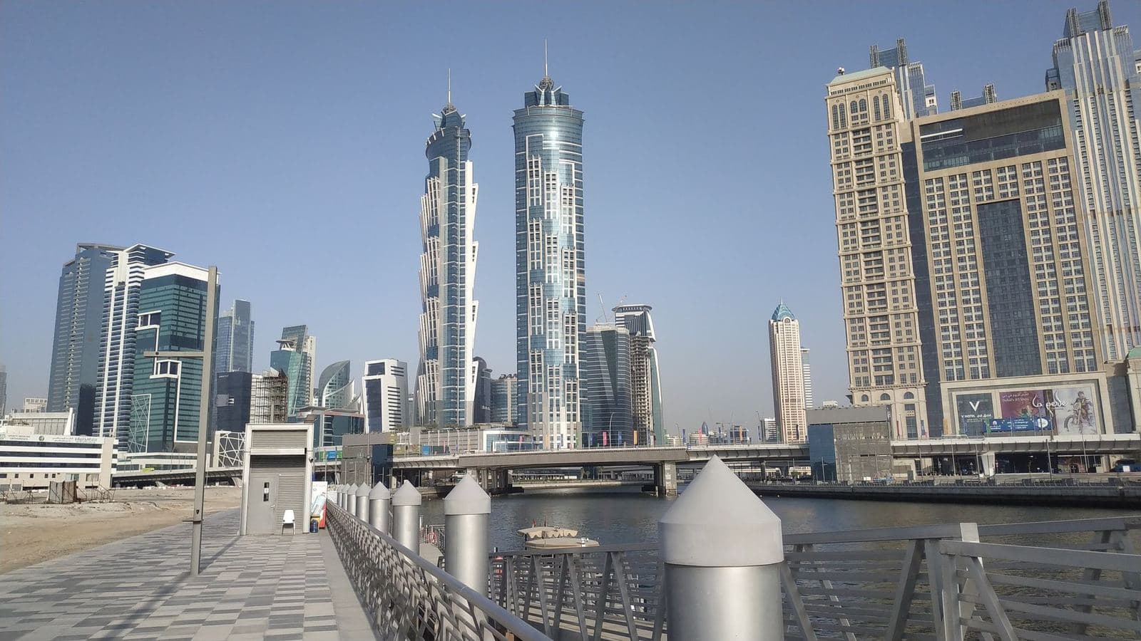 Waterside promenade and footbridge along the Dubai Water Canal with towers of Business Bay behind