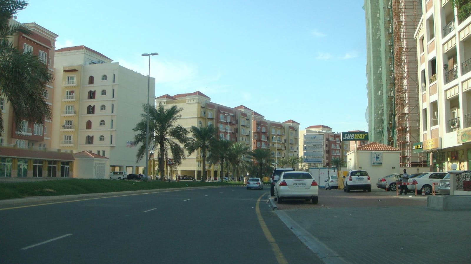 Low rise residential buildings and palm lined street in the Spain cluster of International City, Dubai