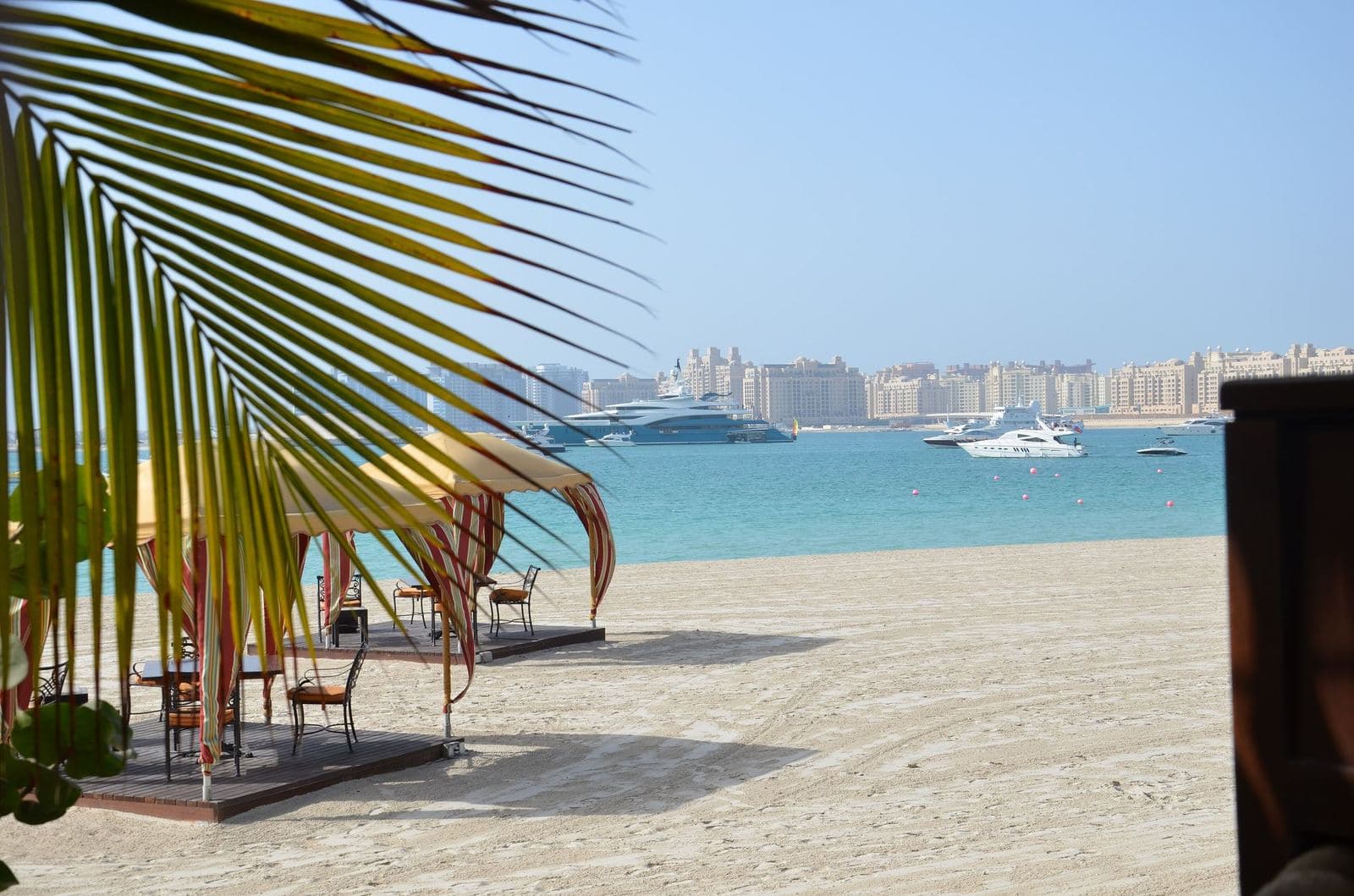 Sandy Al Sufouh beach with a shaded seating area and a view across the water to Palm Jumeirah