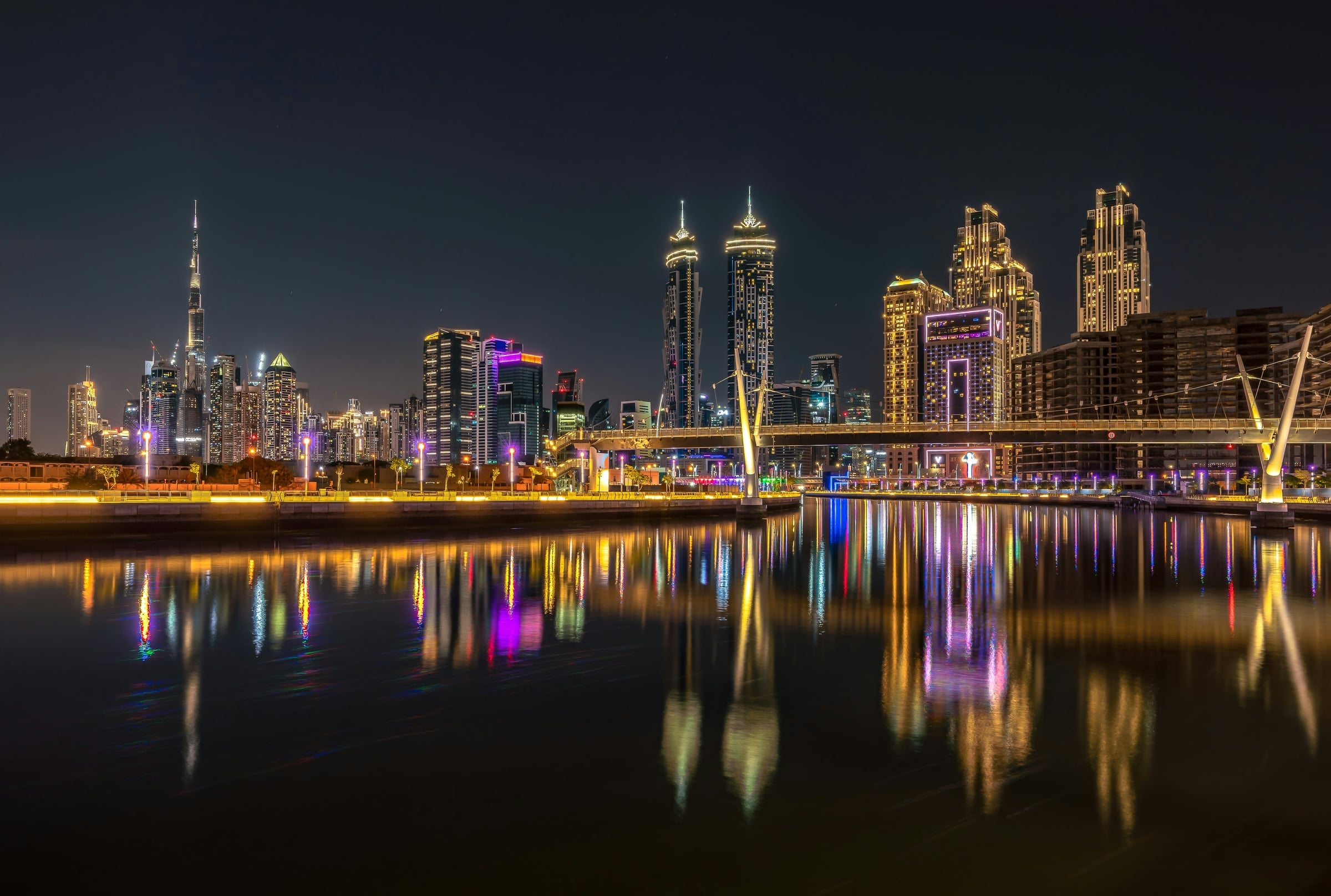 The Dubai Water Canal in Business Bay at night, with the Burj Khalifa and illuminated towers reflected in the water