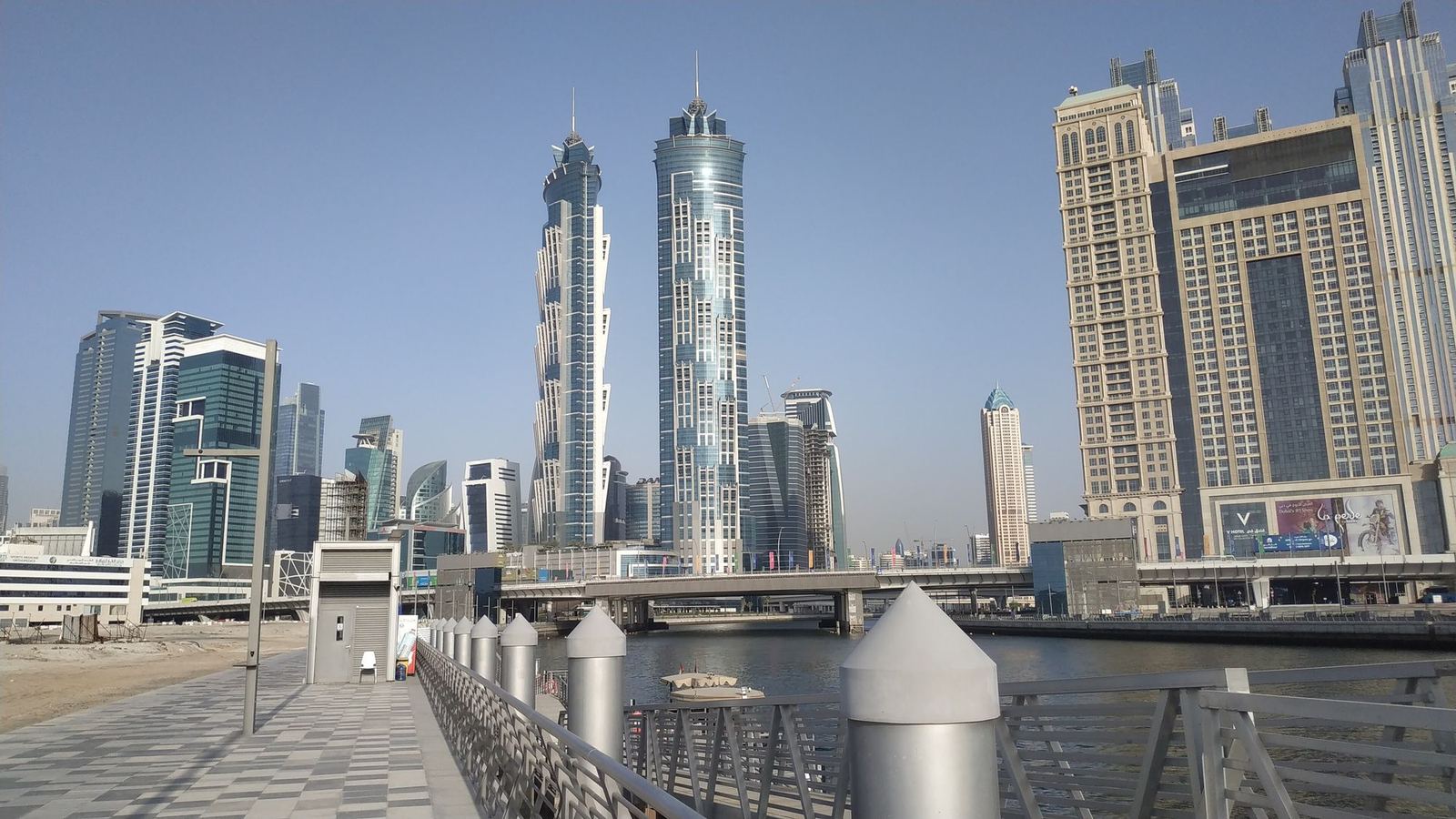 Waterside promenade and footbridge along the Dubai Water Canal with towers of Business Bay behind