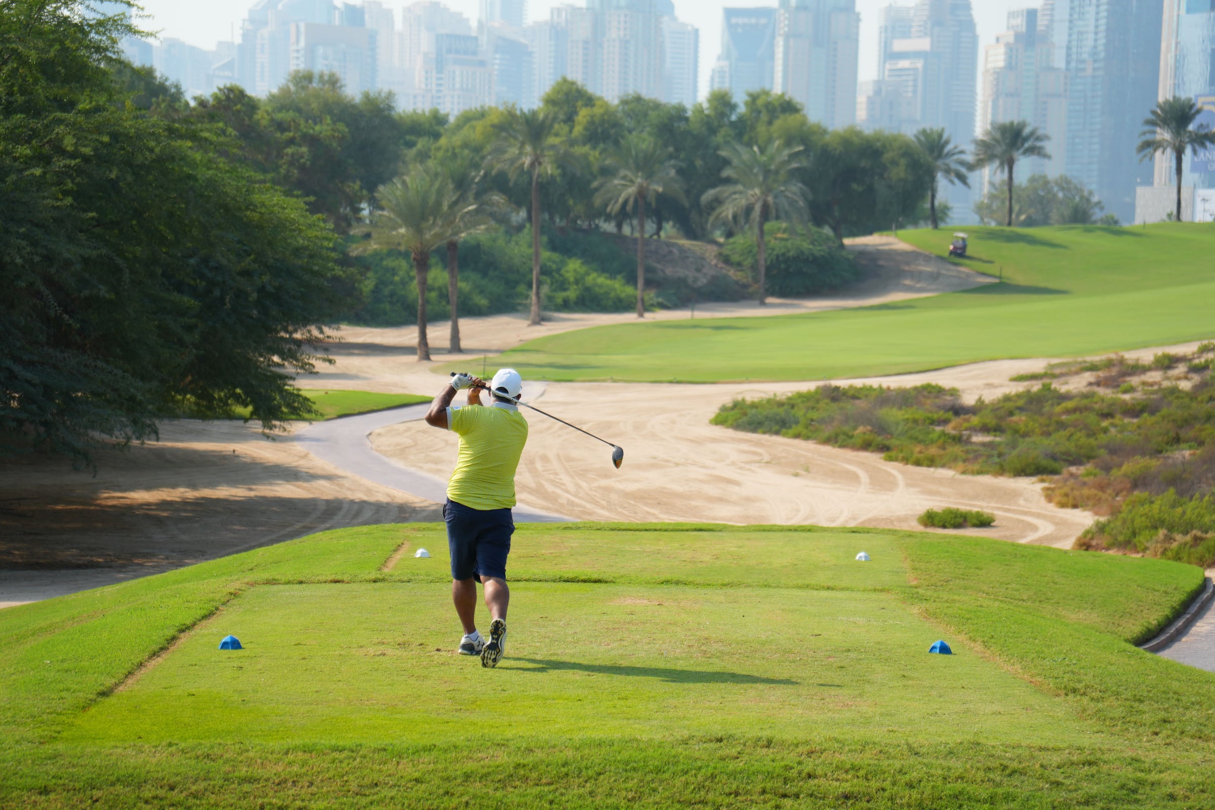 A golfer tees off on a Dubai fairway with the city skyline behind