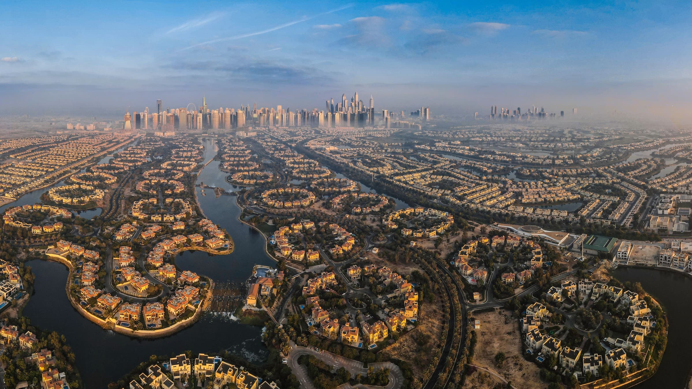 Aerial view of the Jumeirah Islands villa clusters set in their lakes, with the Dubai Marina and JLT skyline beyond