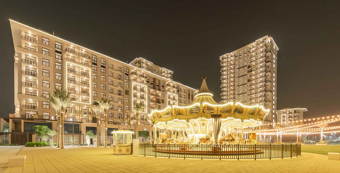 Illuminated carousel in Town Square Park with apartment buildings of Town Square Dubai behind, in the evening